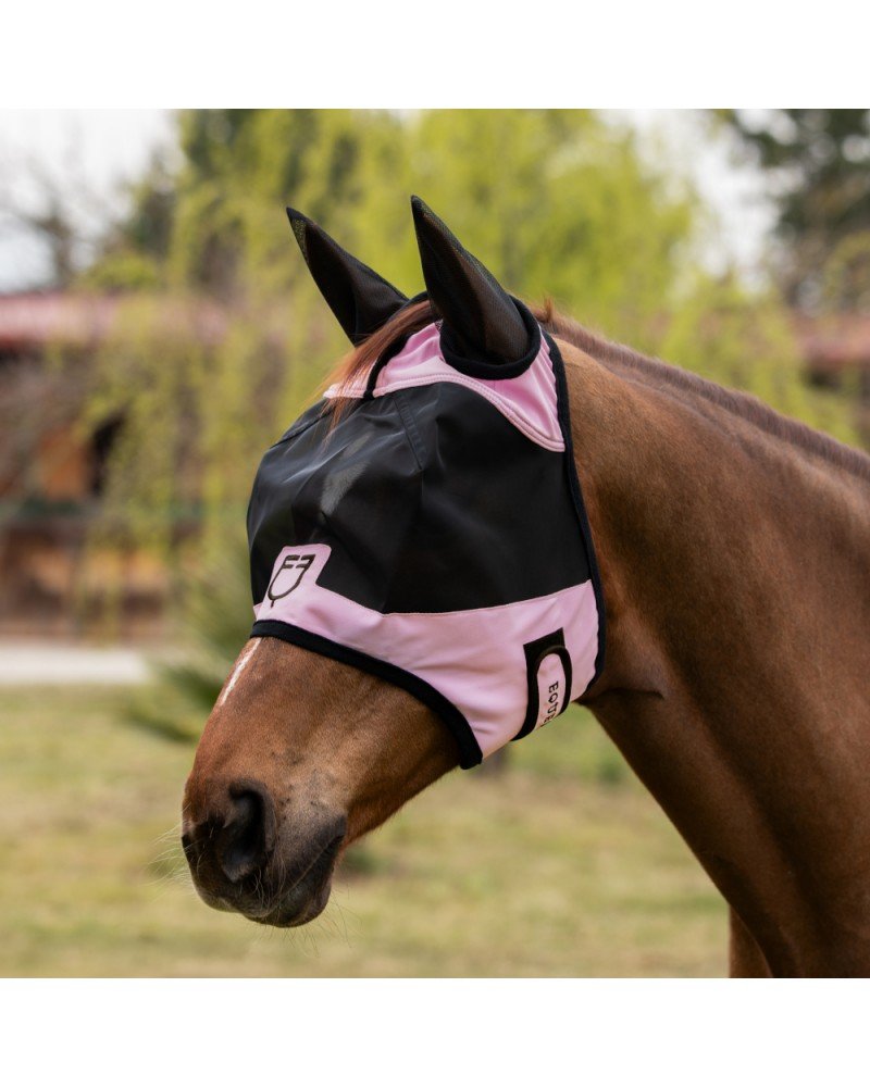 Licol/masque de protection rose et noir sur un cheval brown, tête en vue, fond équestre, logo visible.